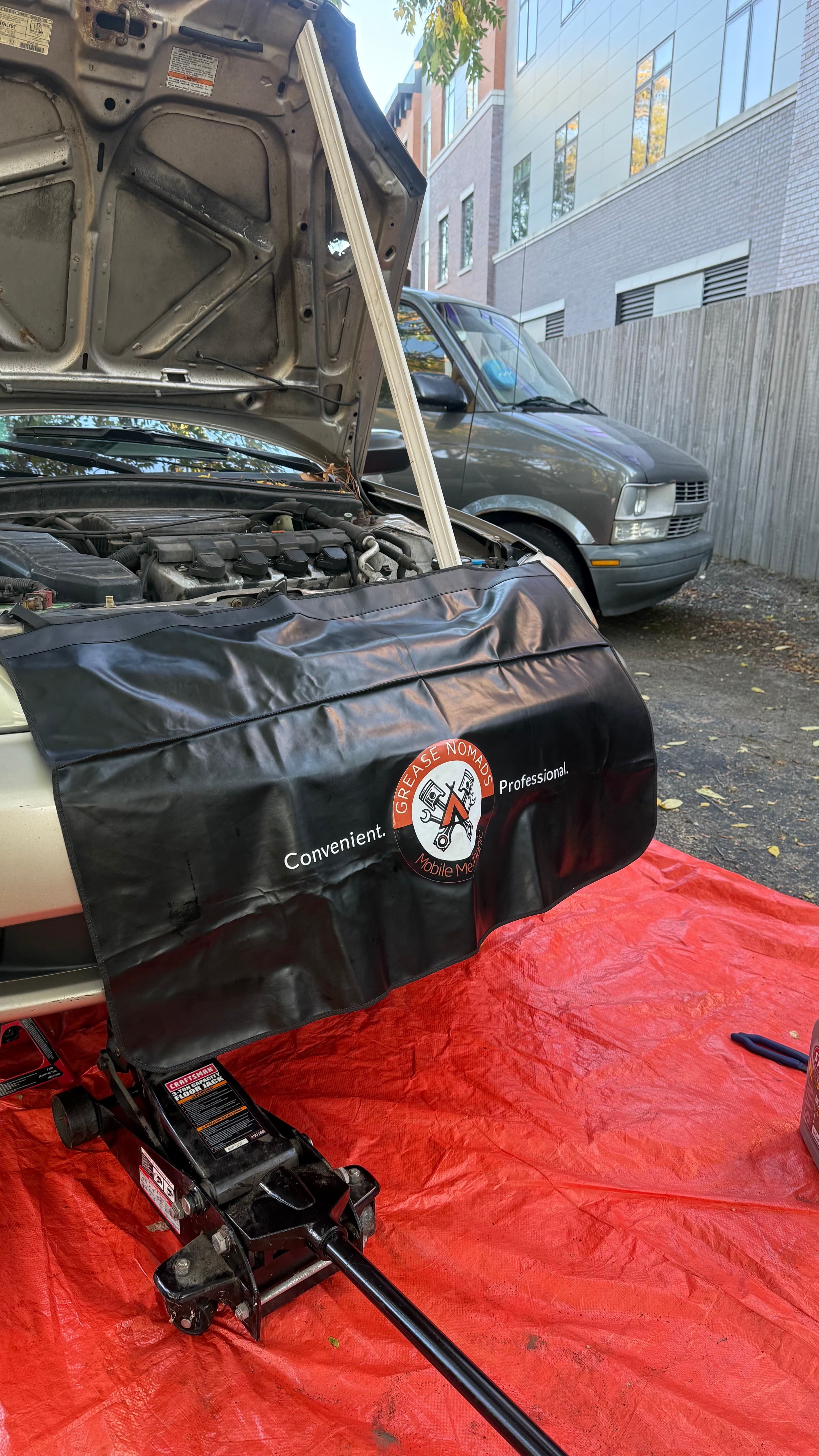 Vehicle with its hood open above a floor jack and protective ground covering during mobile service