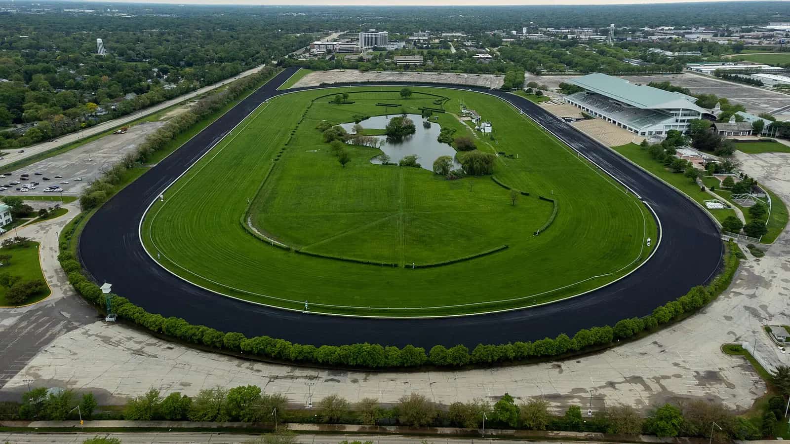 Former Arlington International Racecourse viewed from the east after its final season, with the complete track, grandstand, rail corridor, and surrounding village visible