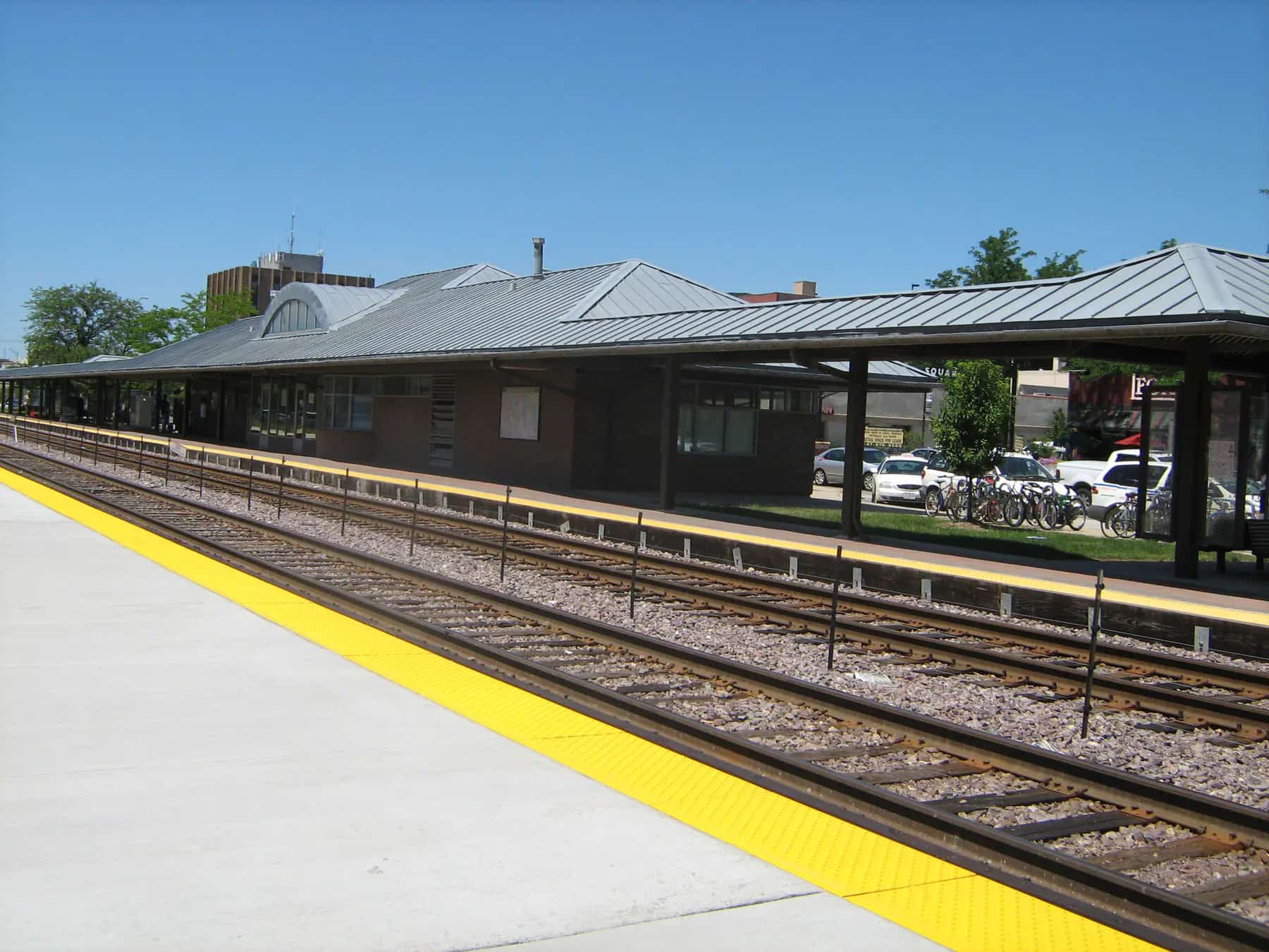 Complete view of the Des Plaines Metra station, platforms, tracks, and surrounding downtown buildings at 1501 Miner Street